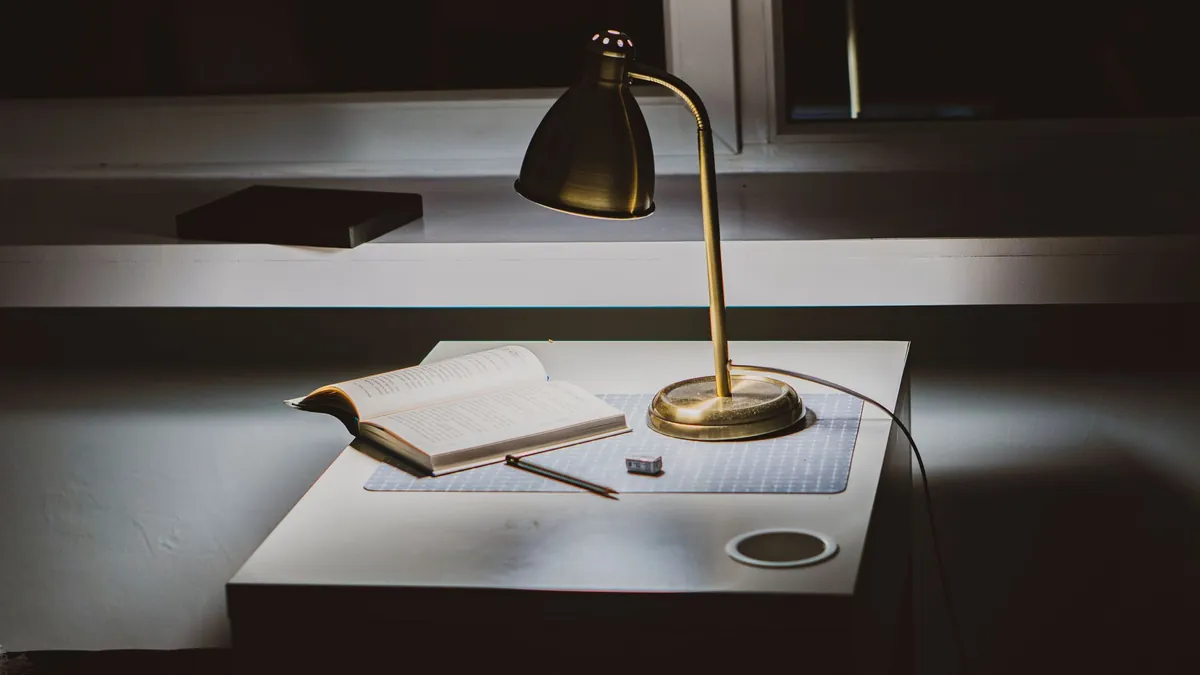 Brass desk lamp lighting an open book on a dark desk