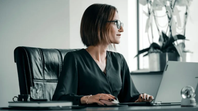 Professional in glasses working at an office desk with a laptop and leather chair