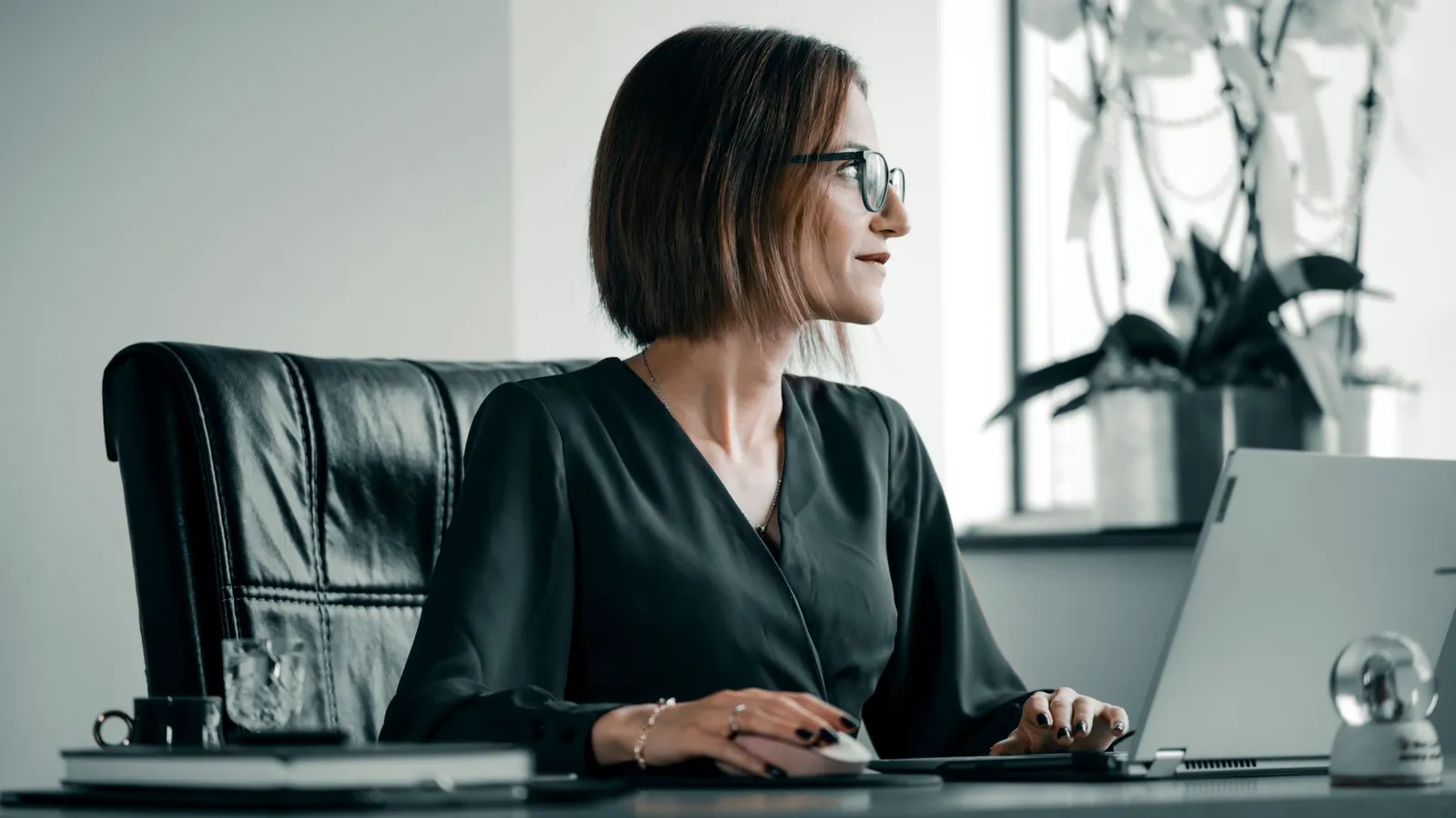 Professional in glasses working at an office desk with a laptop and leather chair