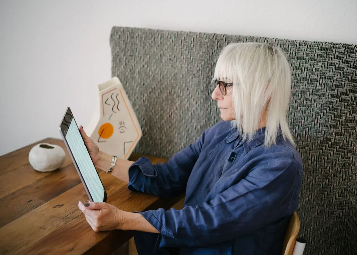 Stylish senior woman in a denim shirt reading on a tablet in a calm, sunlit home