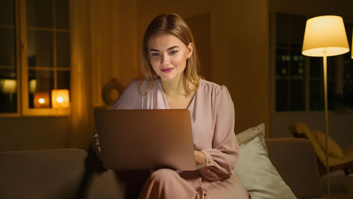Woman reviewing her inbox on a laptop under a warm floor lamp