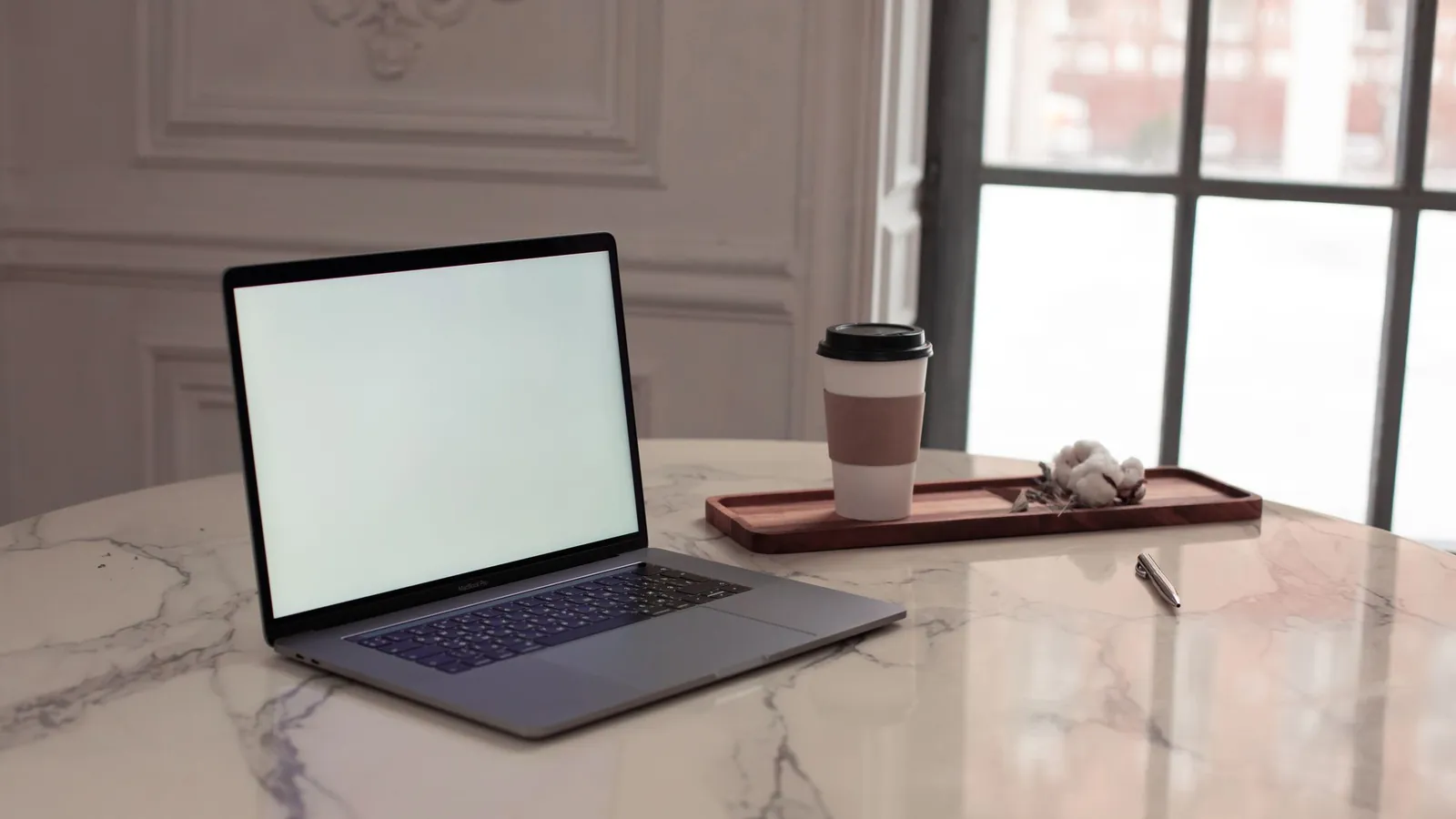 Laptop on a marble table beside tall windows in an elegant room