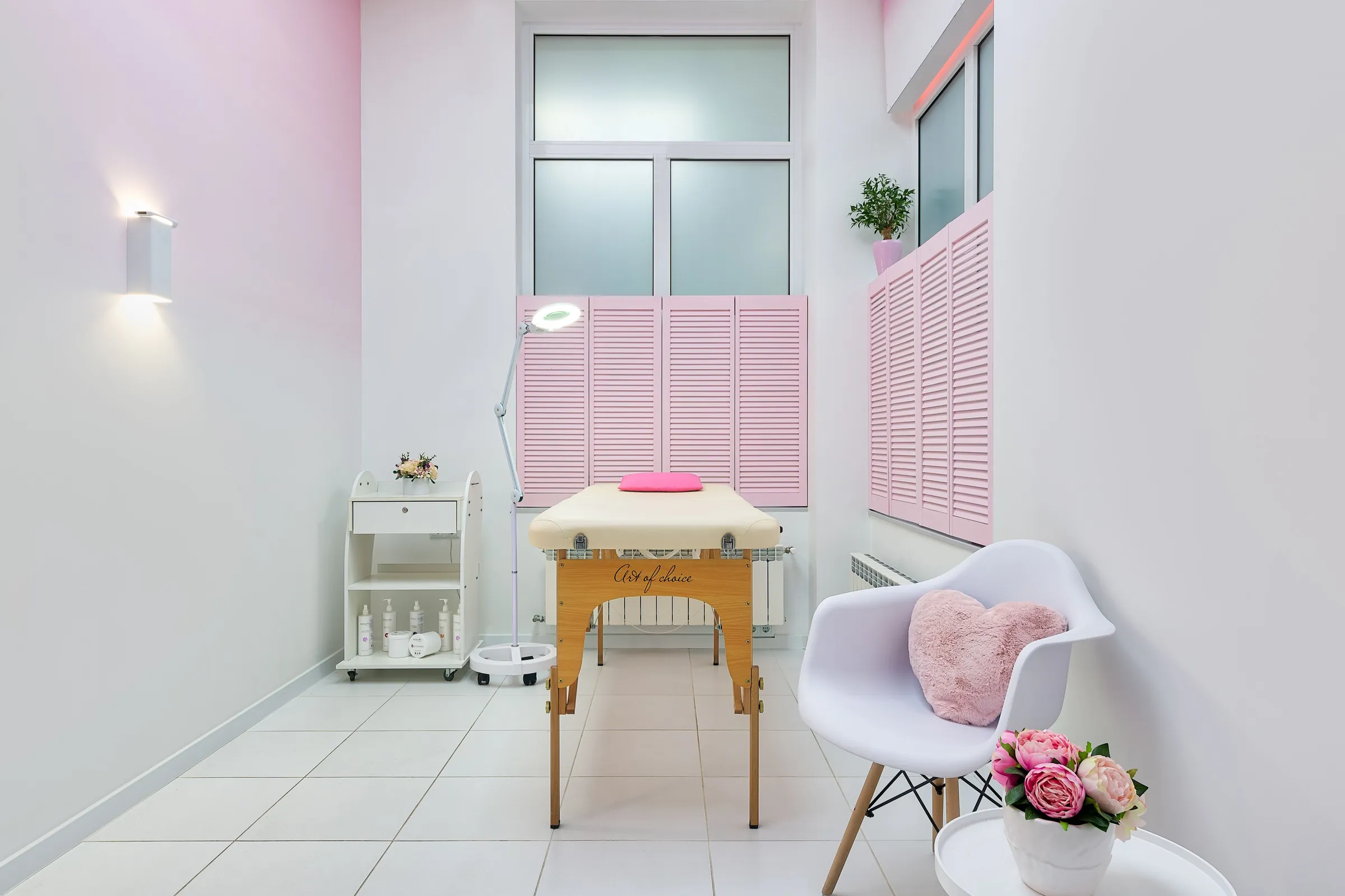 Bright aesthetic treatment room with a treatment bed, pink accents and daylight from a tall window