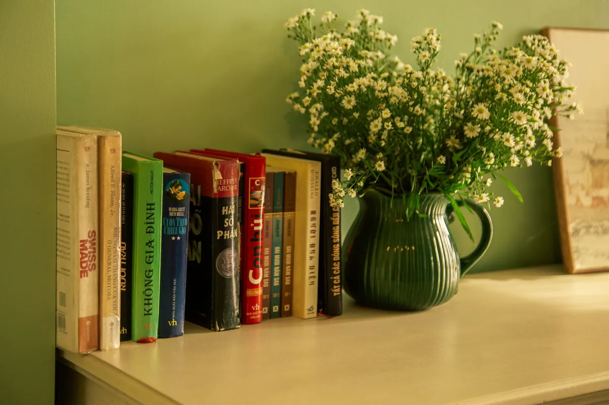 Green ceramic jug of white flowers beside a row of old books