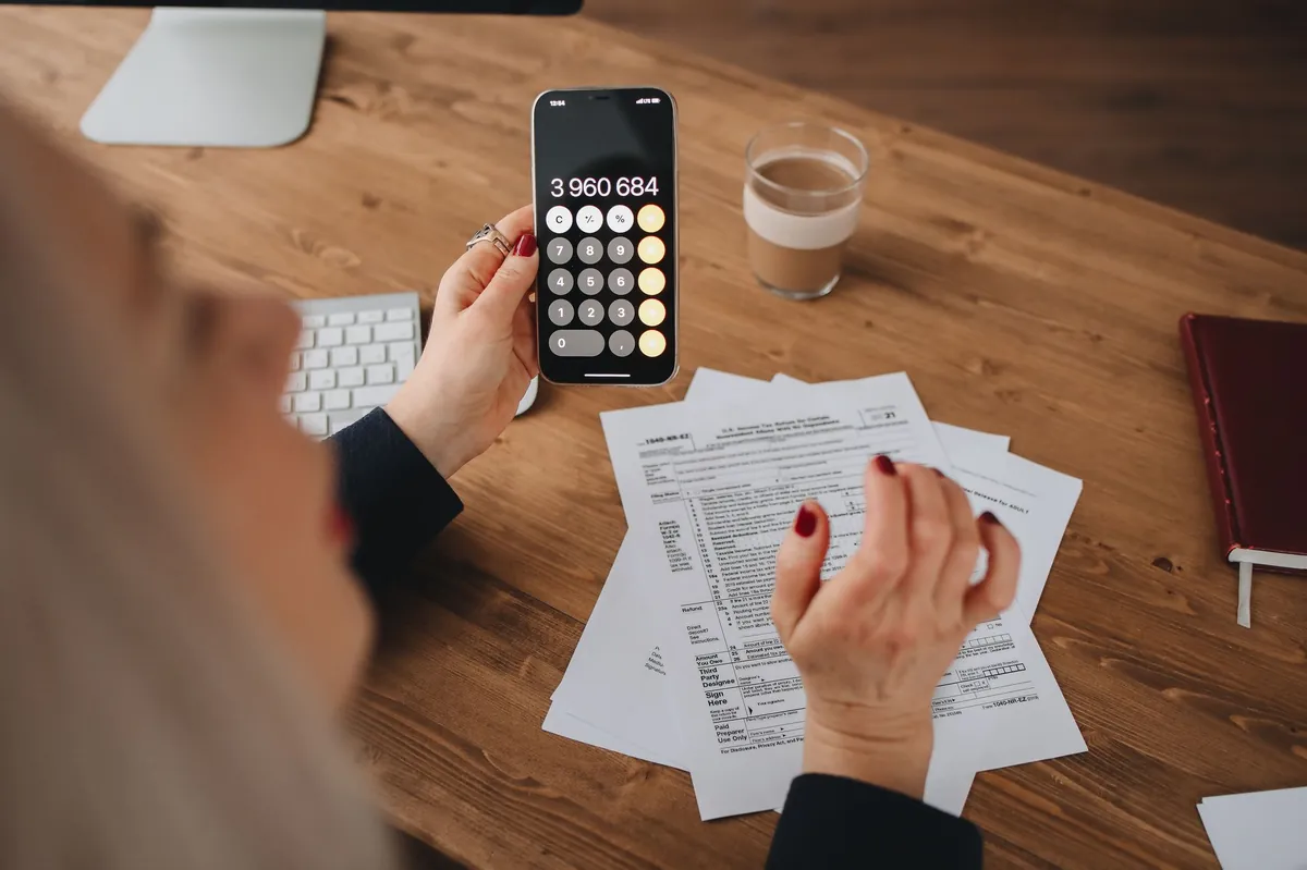 Billing lead calculating figures on a smartphone while reviewing paperwork