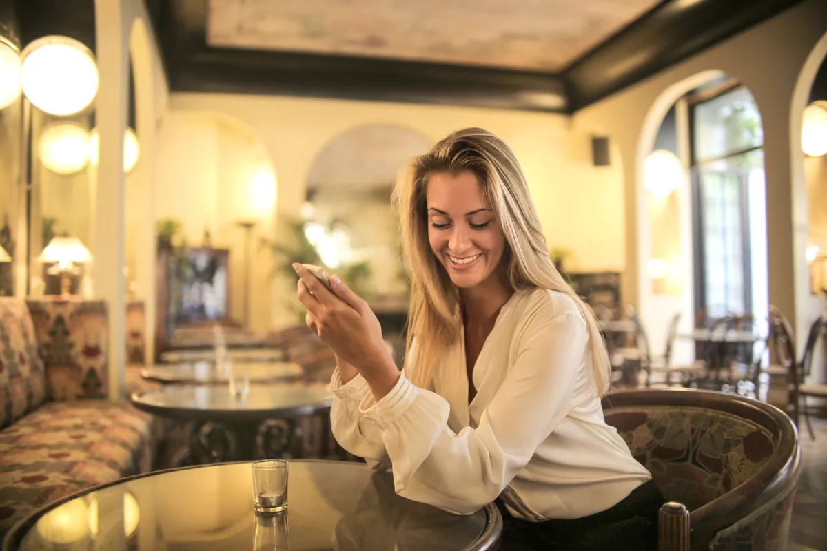 Woman in a white blouse using her phone at a round marble table in an elegant room