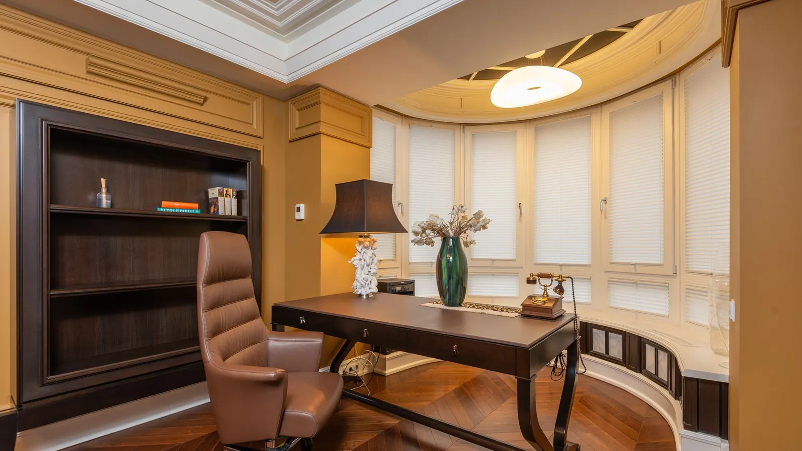 Wood-paneled study with a leather desk chair and warm bay windows