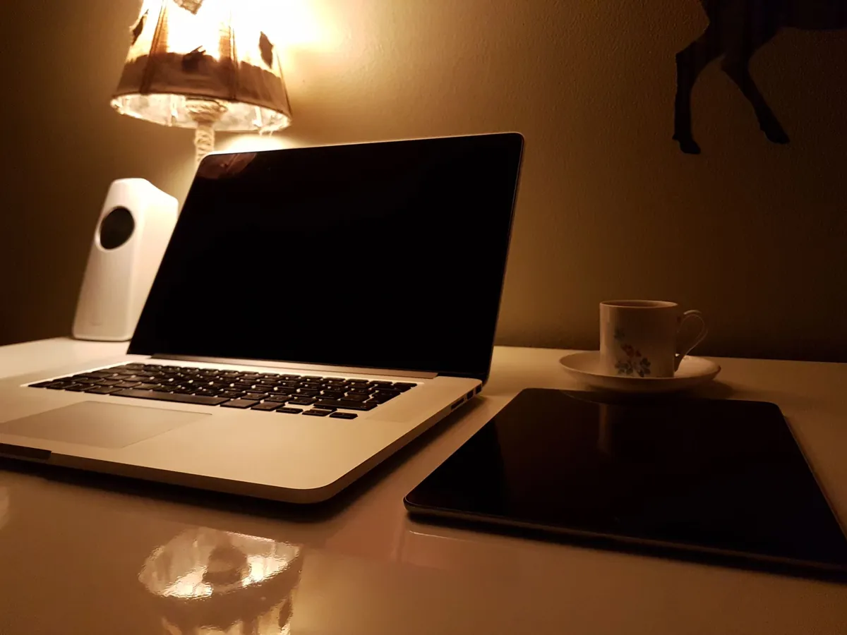 Open laptop and tablet beside a glowing lamp on a warm-toned desk