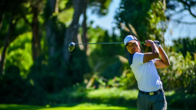 Golfer in a white polo finishing a full swing on a lush, sunny course