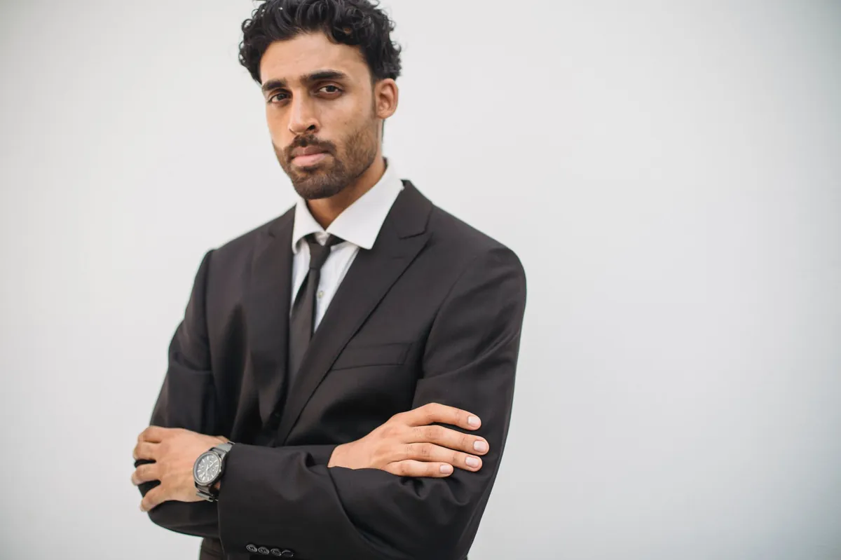 Confident young man in a tailored black suit with arms crossed