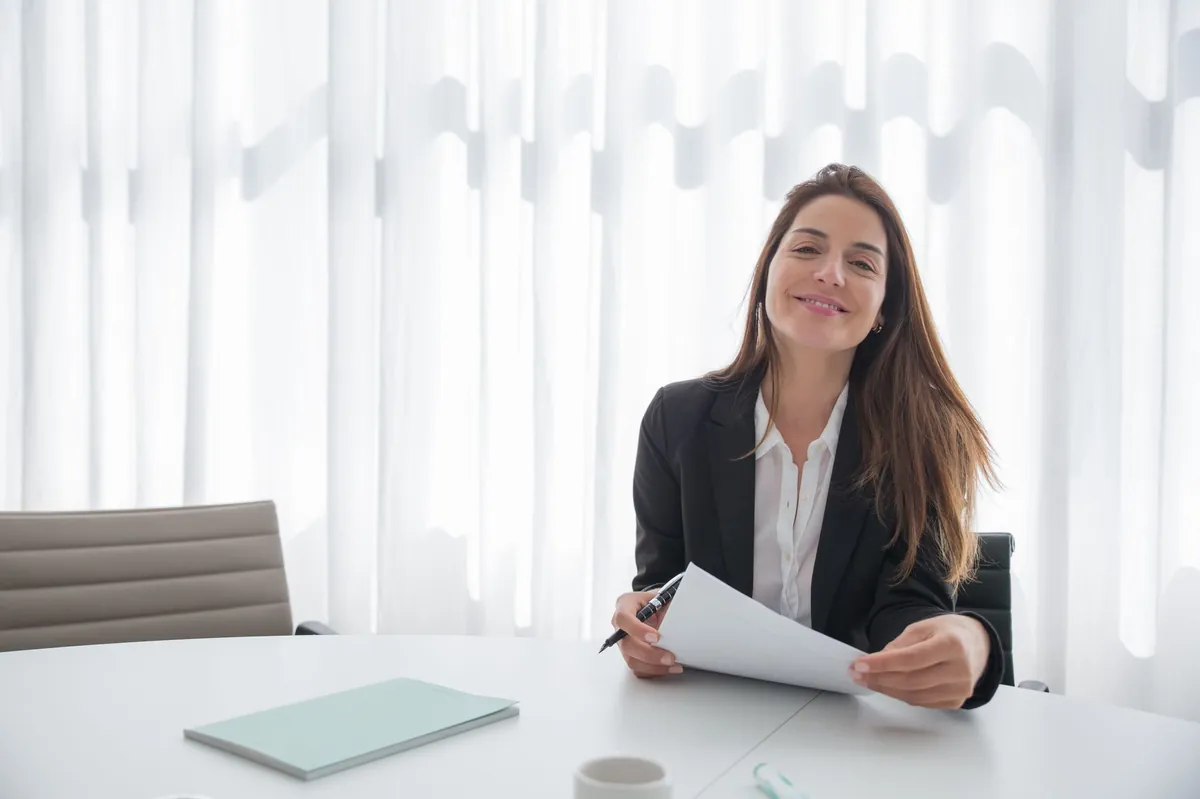 Smiling businesswoman in a blazer reviewing a printed report at an office table