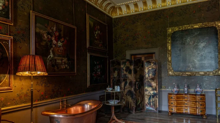 Dark gallery with old master paintings, a gilded frame and a red-shaded lamp