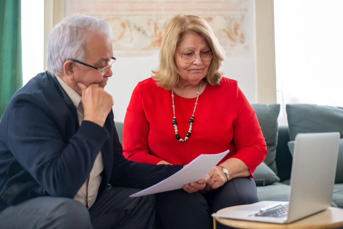 Polished couple reviewing paperwork together on a sofa in a warm, elegant home