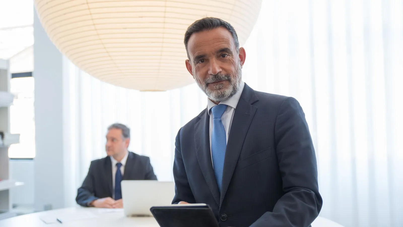 Two businessmen meeting in a modern office, one holding a tablet