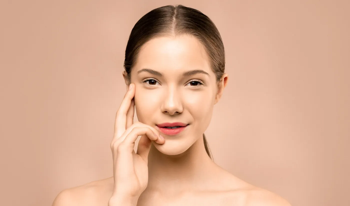 Smiling aesthetic patient with radiant, glowing skin against a warm blush backdrop