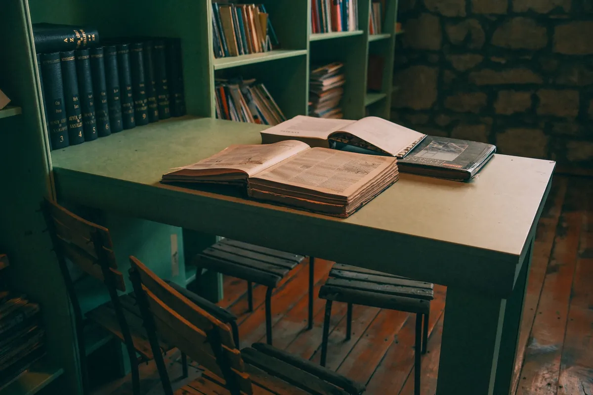 Green study table with open leather-bound books and library shelves