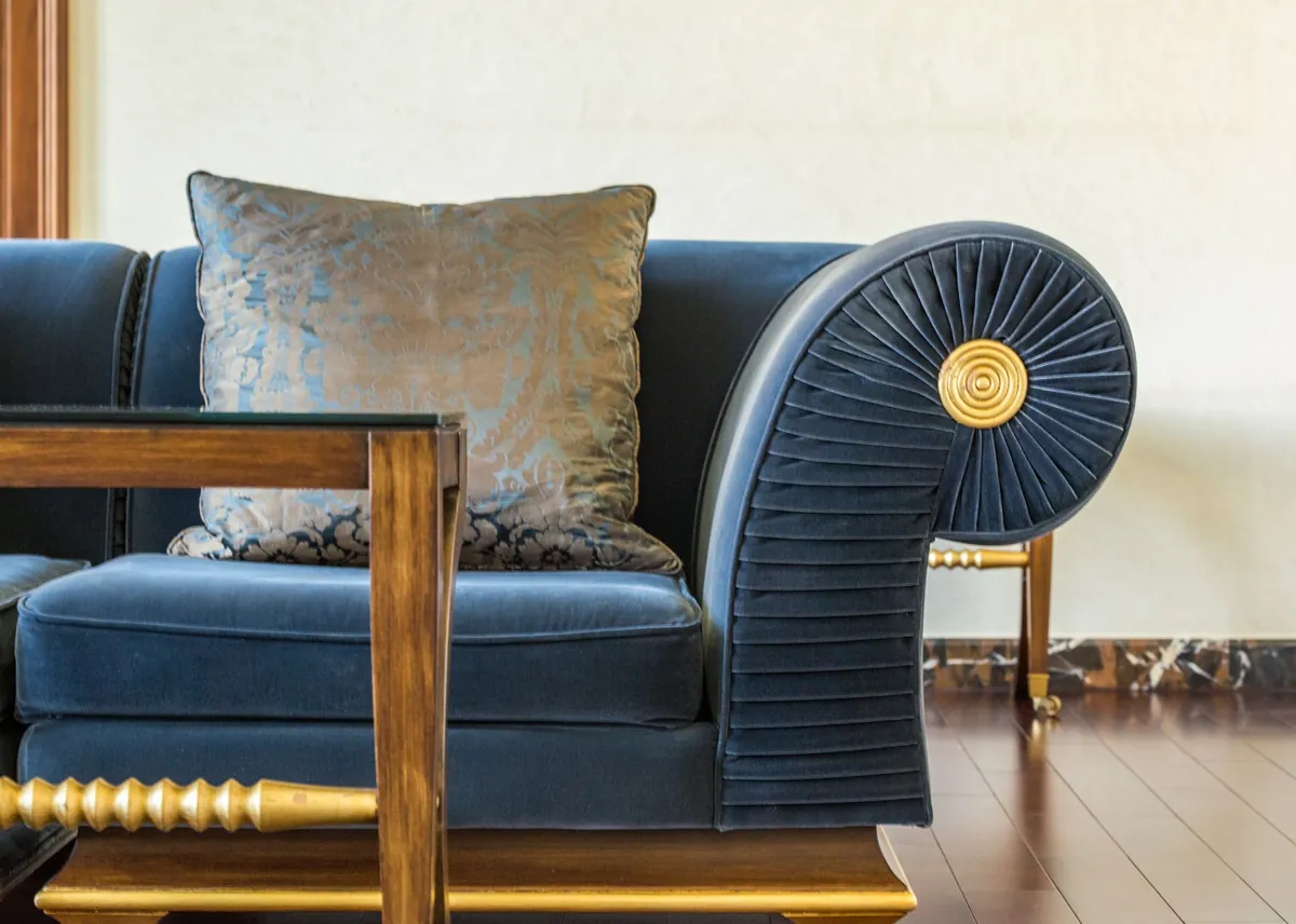 Navy velvet sofa with a sculpted arm beside a gold-trimmed table