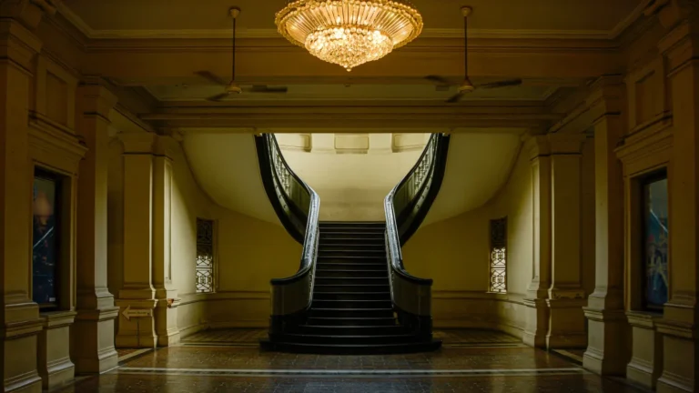 Twin marble staircases rising beneath a crystal chandelier in a stately hall