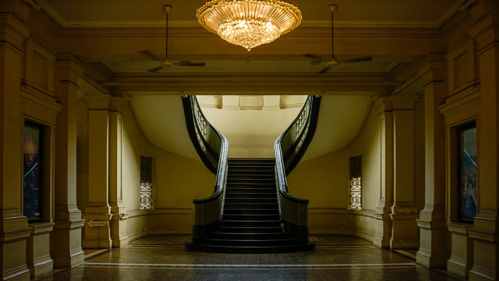 Twin marble staircases rising beneath a crystal chandelier in a stately hall