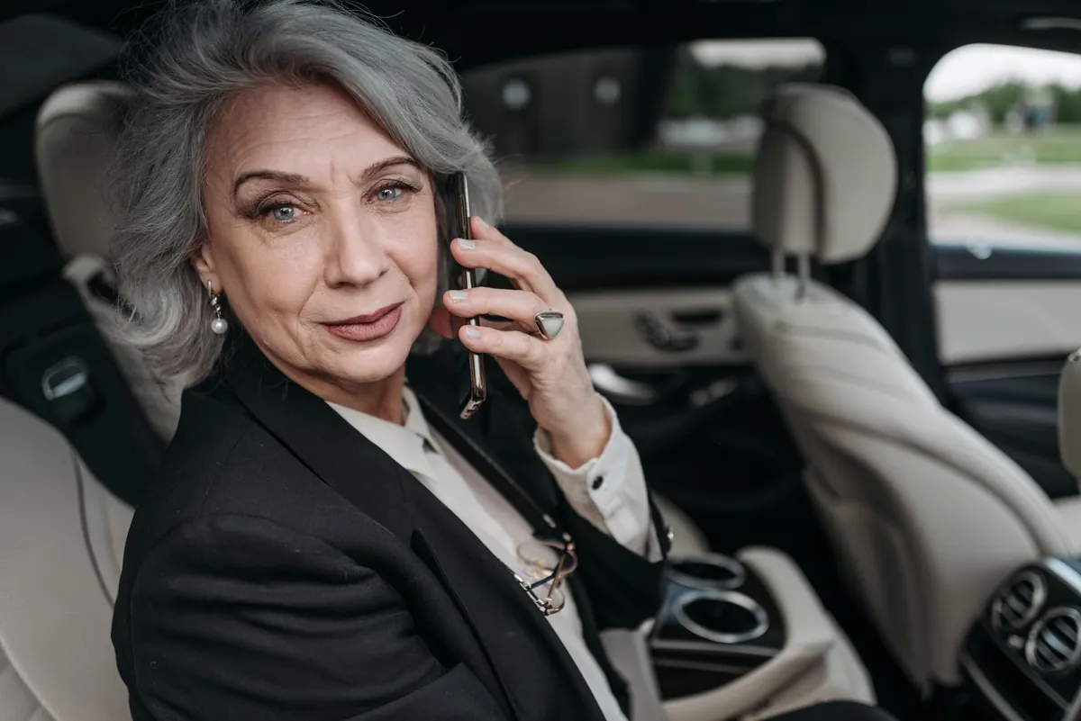 Silver-haired executive in a black suit on a phone call in a luxury car