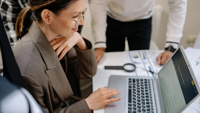 Businesswoman reviewing ad copy on a laptop at a desk while a colleague looks on