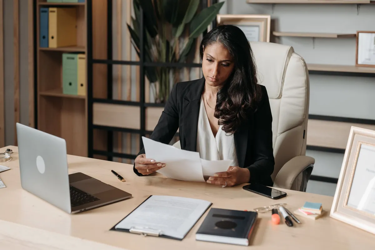 Professional woman reviewing documents at a white desk in a light, modern office
