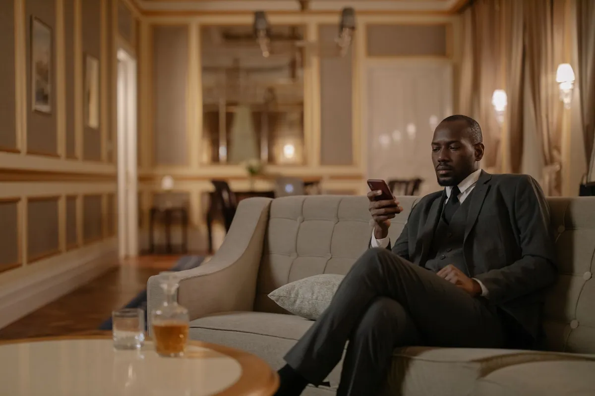 Well-dressed man relaxing with his phone in a warmly lit hotel-style lounge