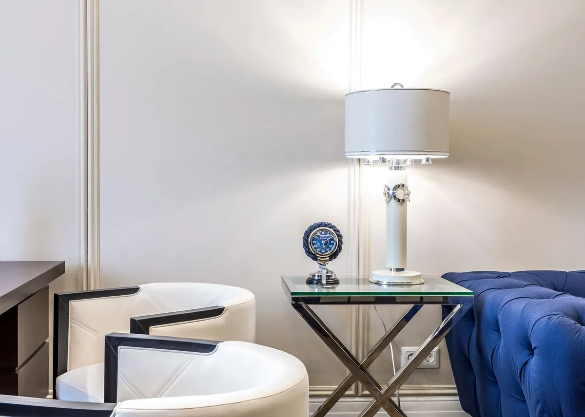Quiet corner with a white armchair, side table lamp and navy velvet sofa