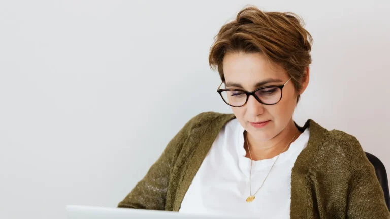 Practice lead in eyeglasses smiling while working on a laptop in a bright office