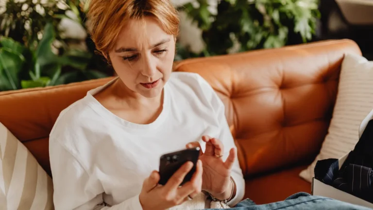Woman reading reviews on her phone while relaxing on a leather sofa