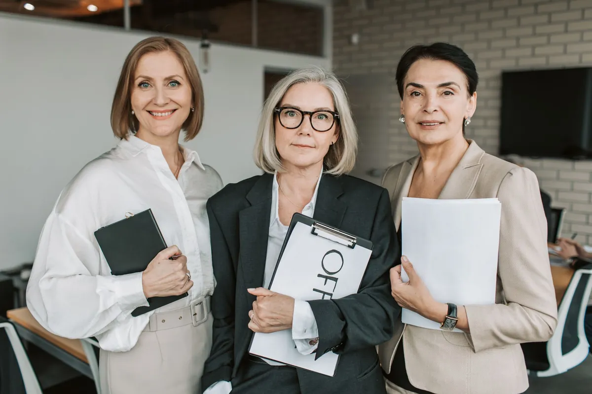 Three confident businesswomen holding papers in a bright, modern office