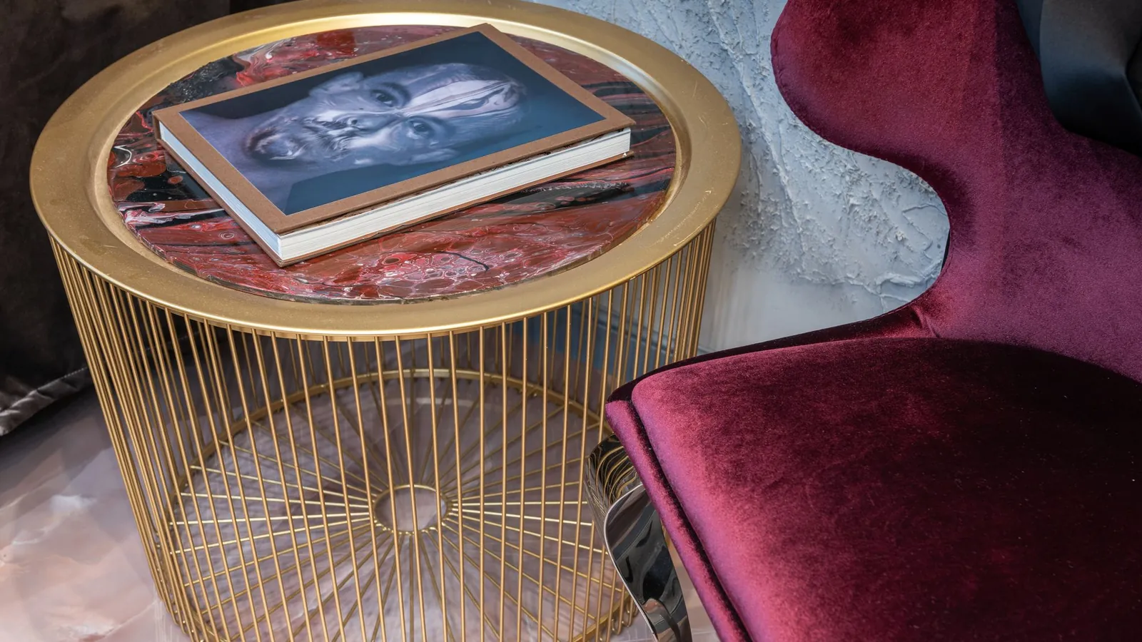 Brass side table holding a book beside a burgundy velvet chair