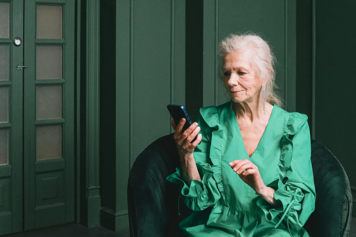 Mature woman in a green dress checking her phone in a dark green paneled room