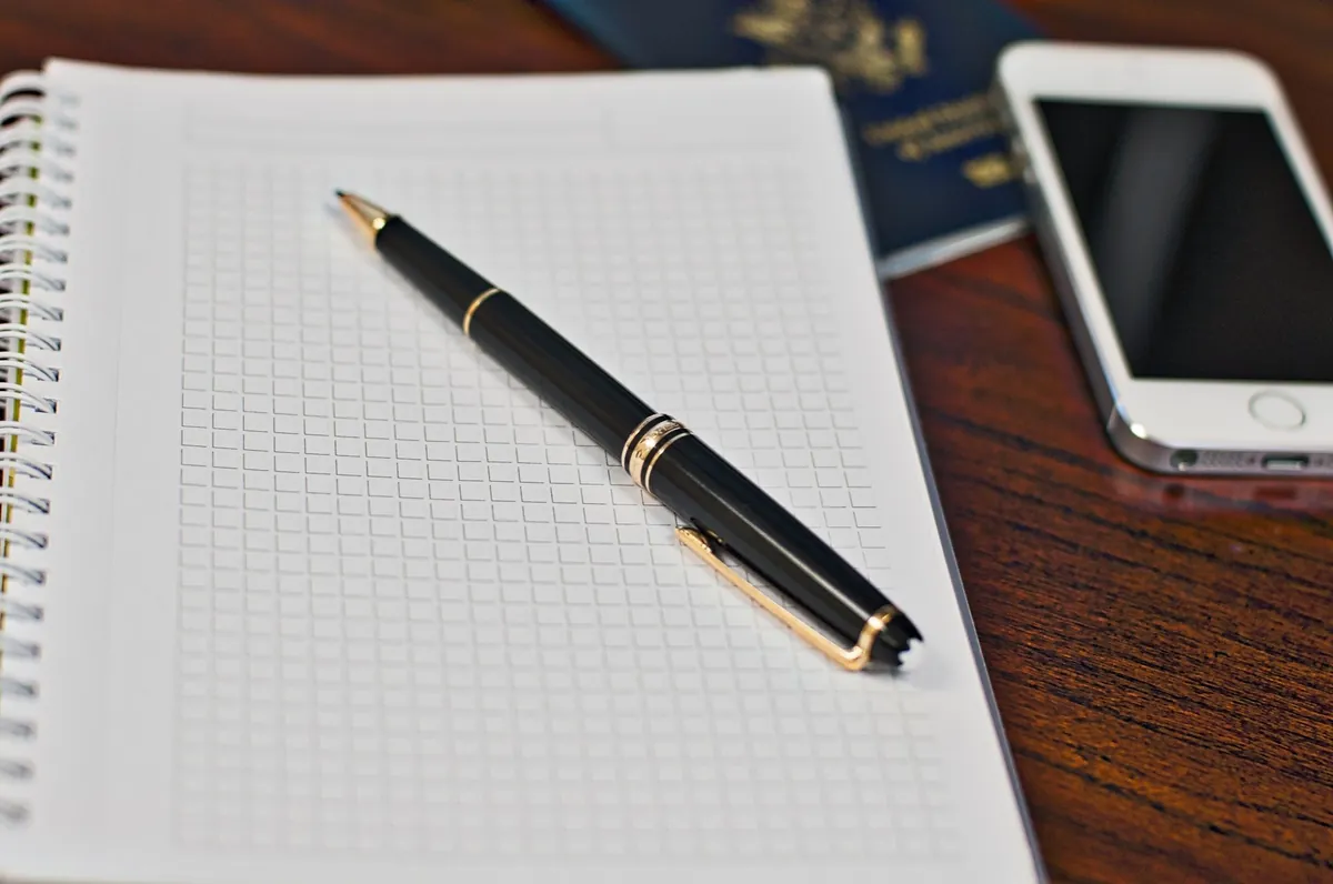 Black and gold pen on a grid notebook beside a smartphone