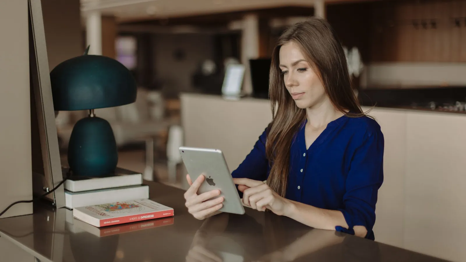 Professional reading reviews on a tablet at a desk lined with books in a modern office