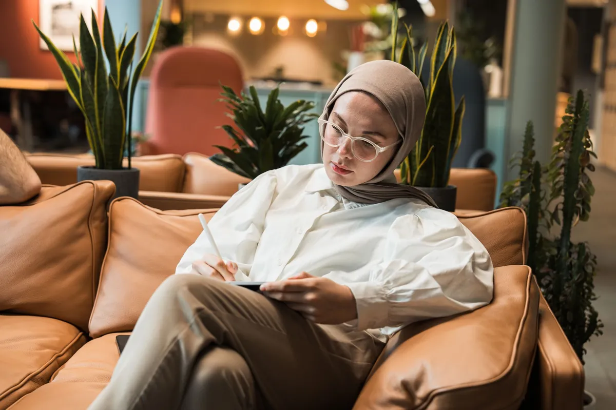 Woman on a leather couch writing notes on a tablet in an elegant interior