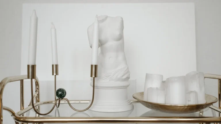 Brass bar cart with a marble bust and candles against a white wall