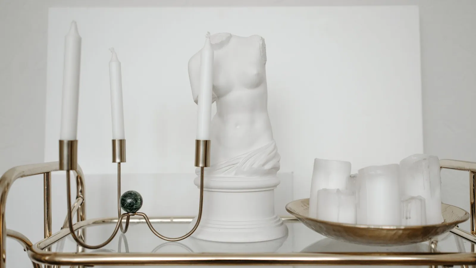 Brass bar cart with a marble bust and candles against a white wall