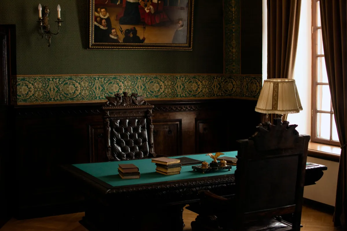 Green baize desk in a dark paneled study with a brass reading lamp