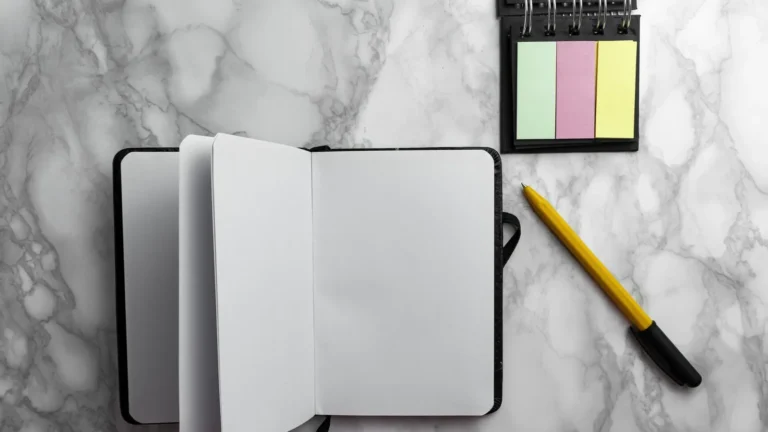 Open notebook, pen and sticky notes on a gray marble desk