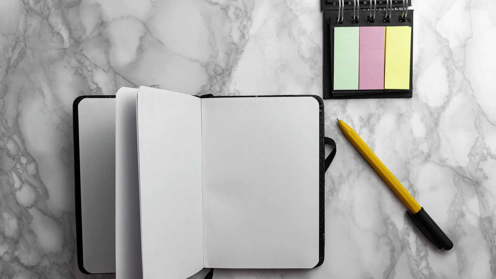 Open notebook, pen and sticky notes on a gray marble desk