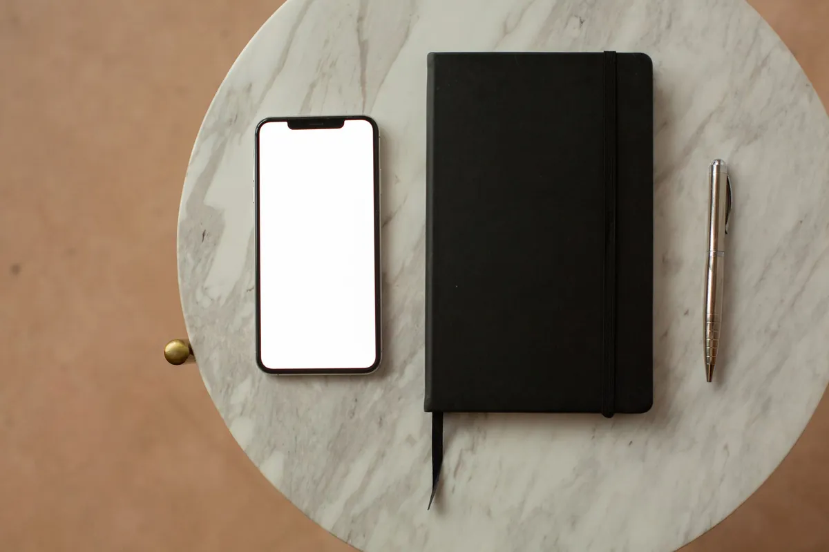 Smartphone, black notebook and pen on a round marble tray