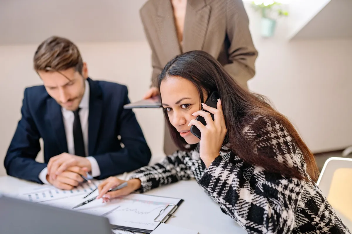 Team meeting with a professional on a phone call while colleagues review plans