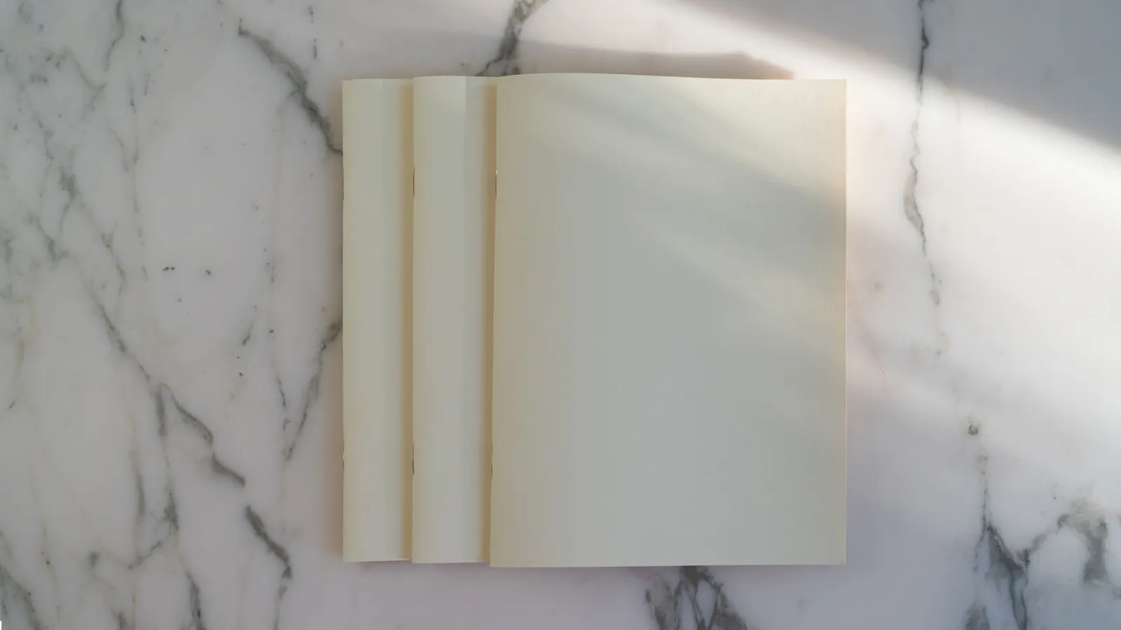 Stack of blank notebooks on a white marble surface in soft light