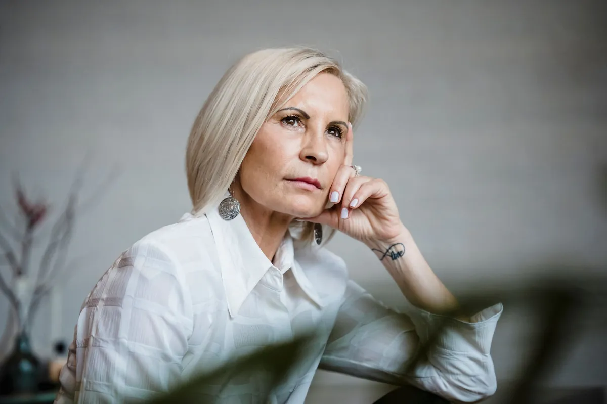 Thoughtful woman with short silver hair in a crisp white shirt, resting her chin on her hand