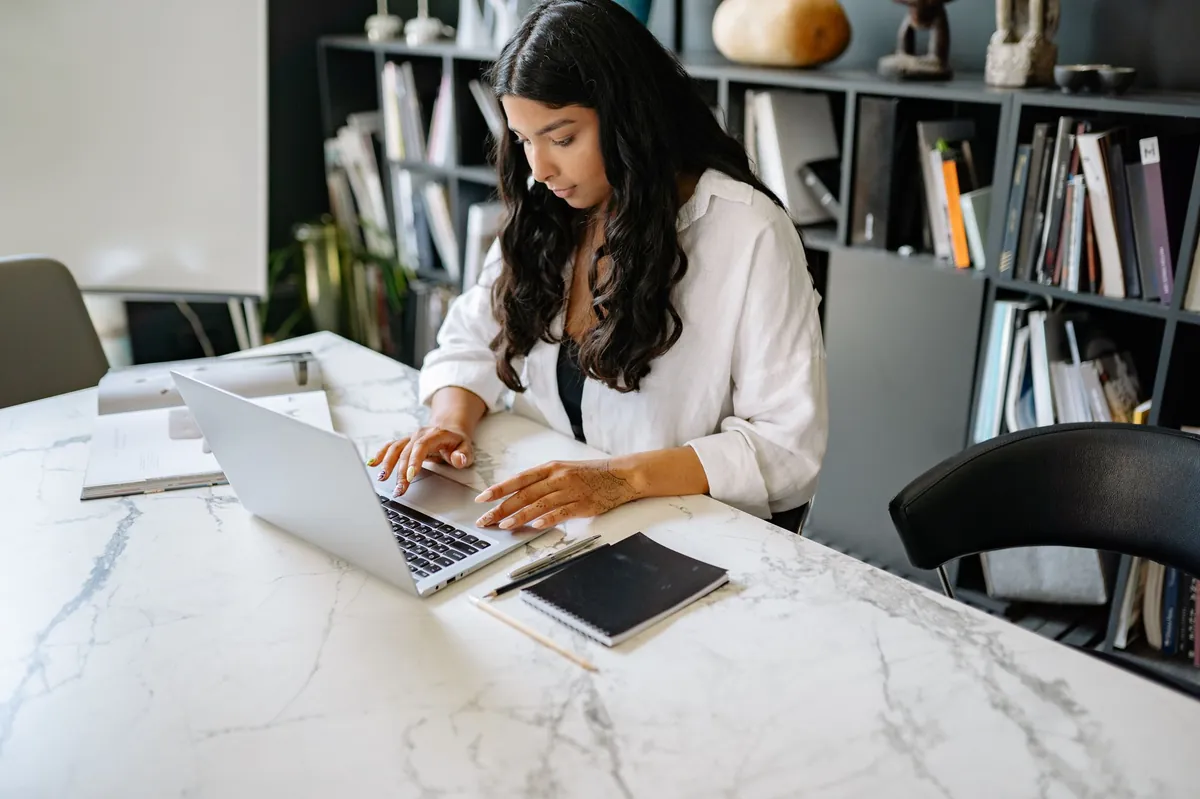 Woman in a white shirt working on a laptop at a white marble desk in a bright office