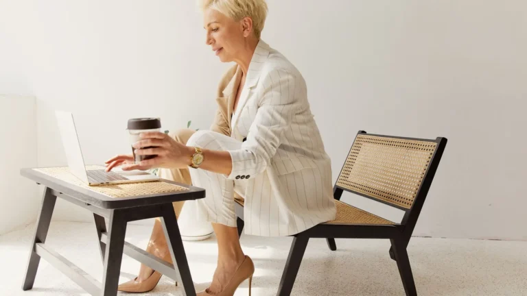 Elegant woman in a white suit reviewing her practice website on a laptop at a light wood desk