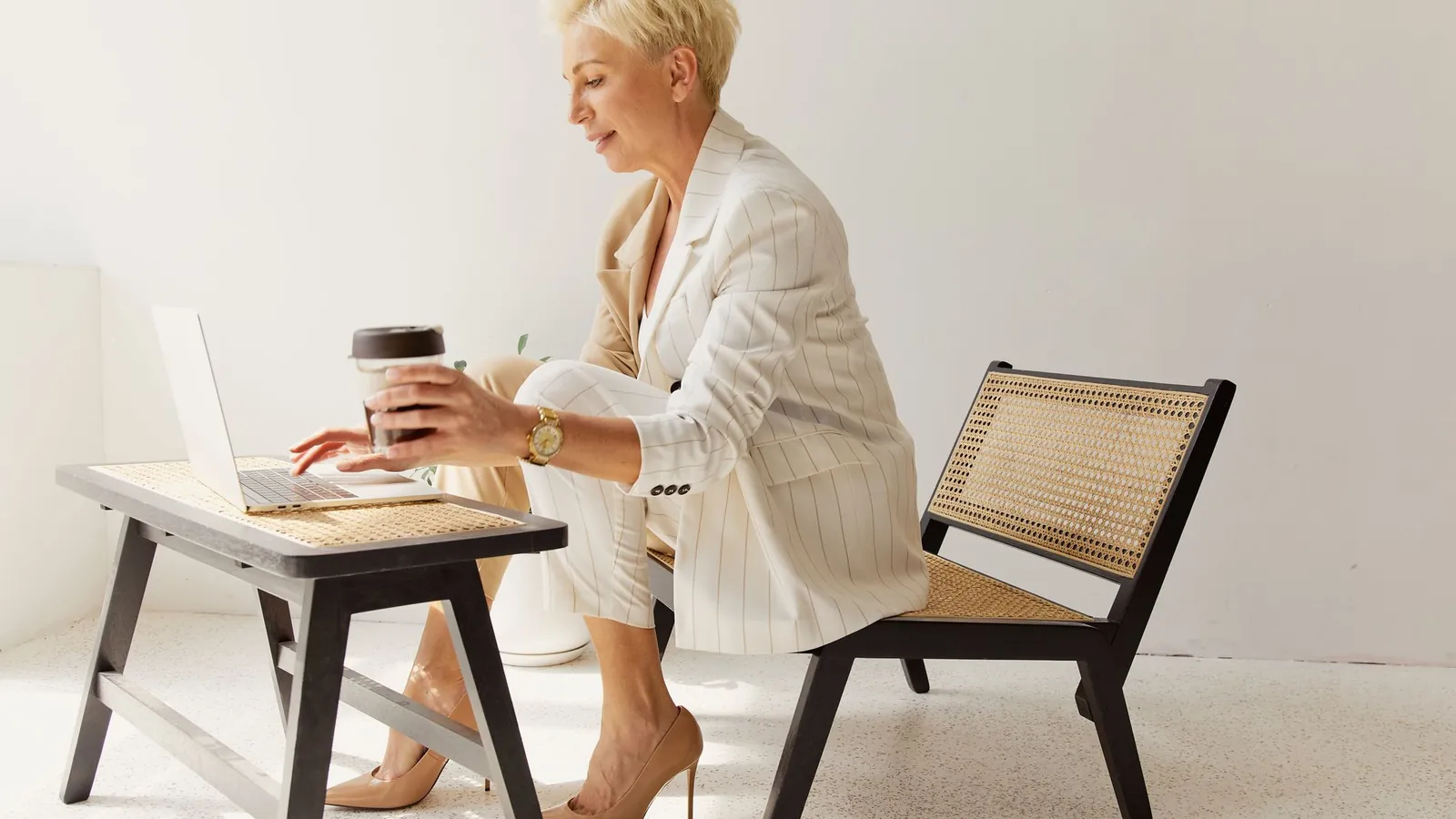 Elegant woman in a white suit reviewing her practice website on a laptop at a light wood desk