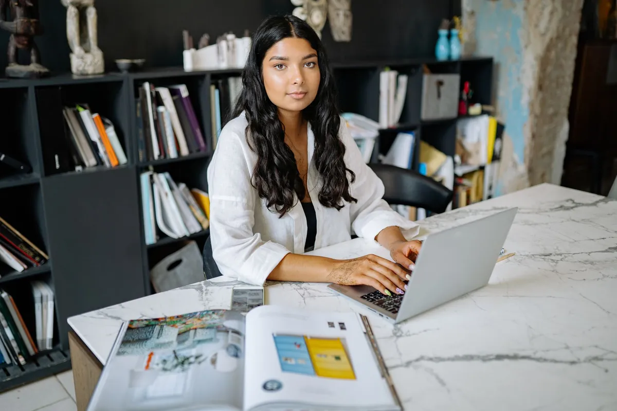 Professional woman working on a laptop at a marble table in a styled office library