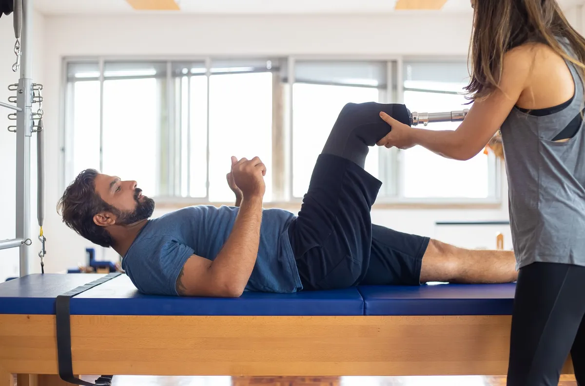 Therapist supporting a patient through a guided stretch on a padded table in a sunny studio
